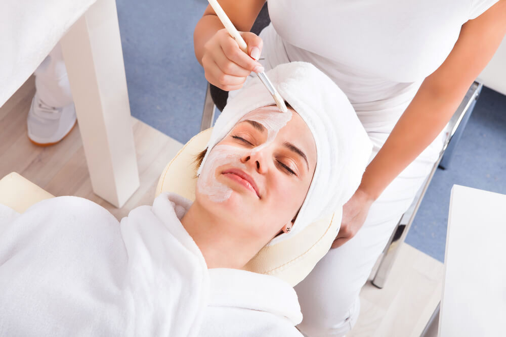 Smiling woman undergoing a facial mask treatment at unknown spa 
