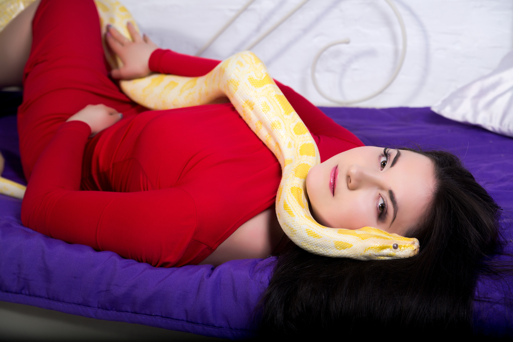 Woman lying on a bed with a snake on her body.